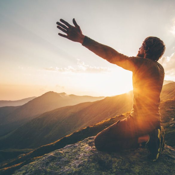 Man praying at sunset mountains raised hands Travel Lifestyle spiritual relaxation emotional concept vacations outdoor harmony with nature landscape